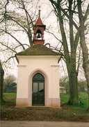 Malá šestiboká stavba okrové         omítky a červené střechy s věžičkou a zvonem obklopená lípami