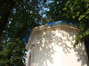 Žlutá fasáda zadní lomenné části kaple, na místo střechy splývá         modrá plachta a prosvítá jasněmodré nebe.